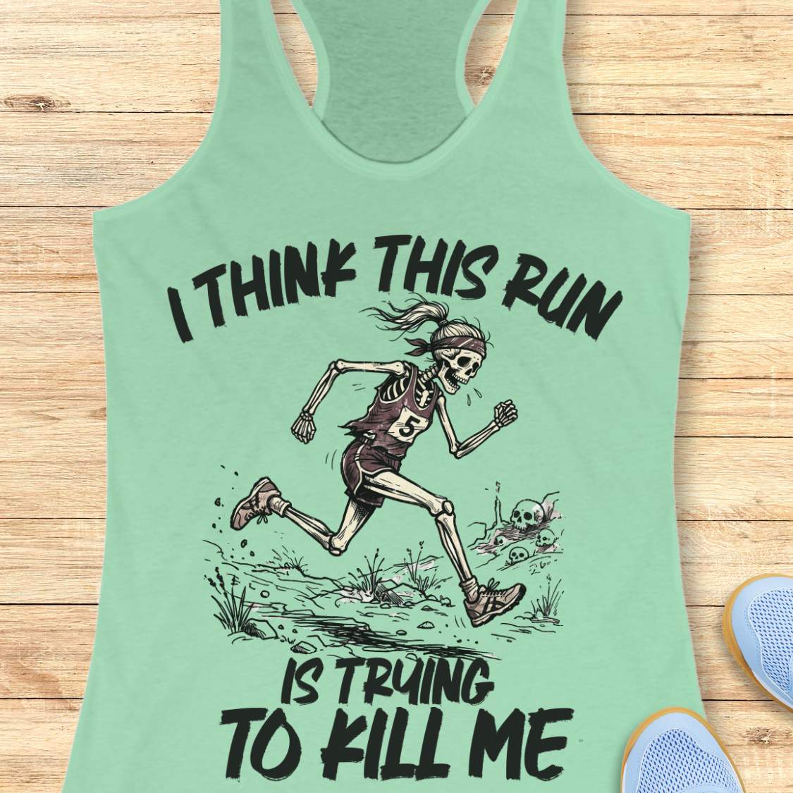 mint tank top with graphic design of a runner skeleton and text 'I think this run is trying to kill me', on a wooden surface