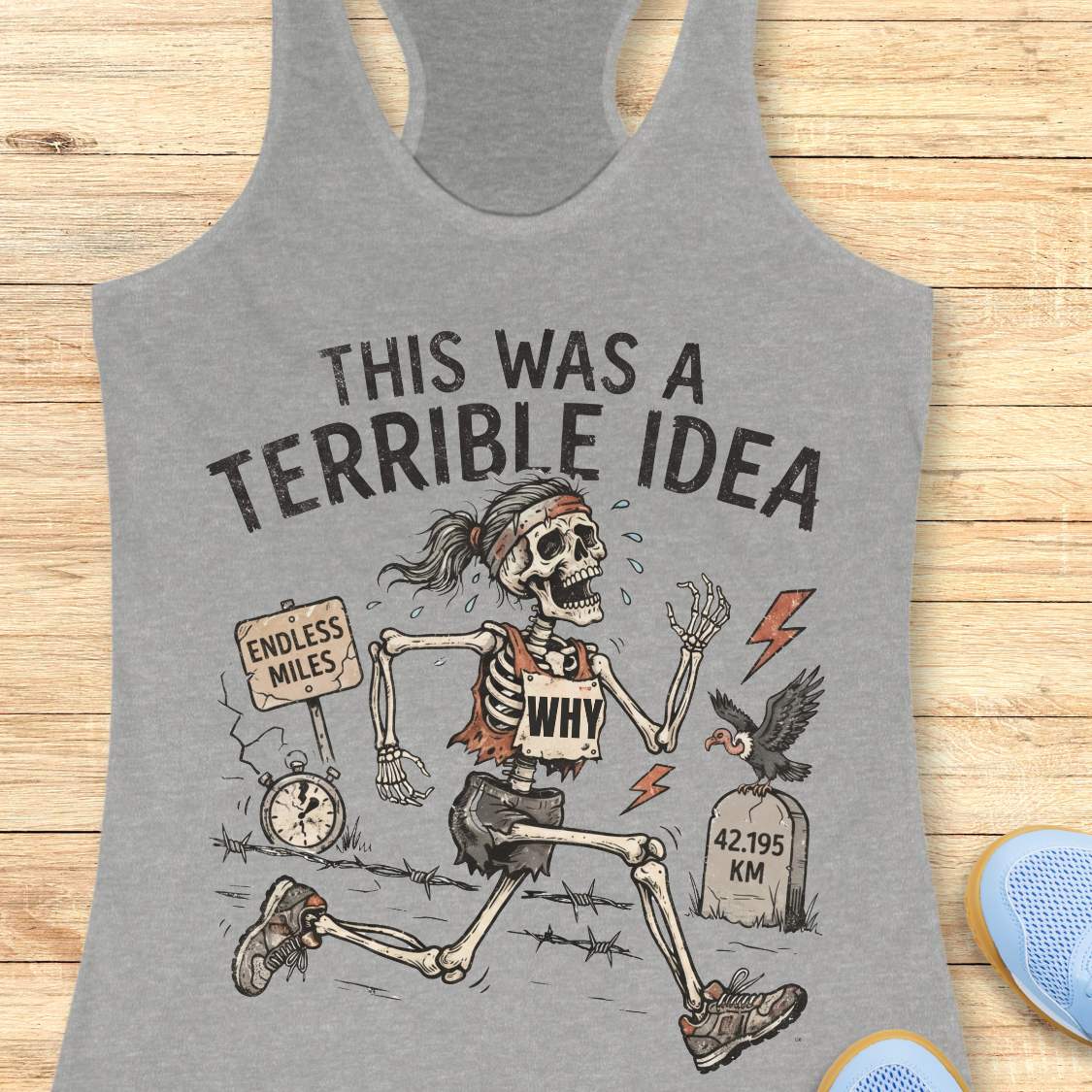 grey tank top with a running skeleton and text 'This was a terrible idea', on a wooden surface