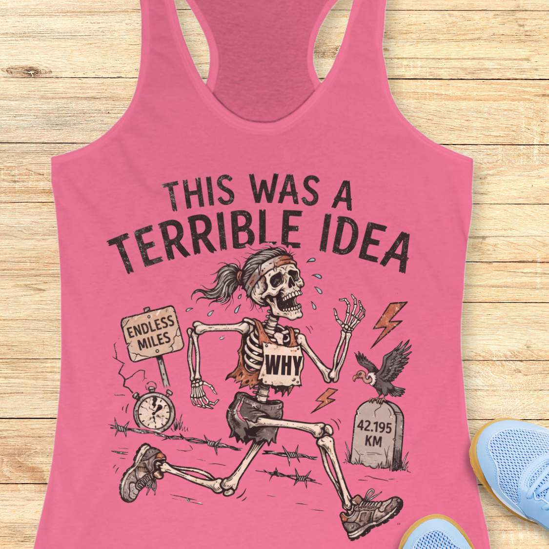 pink tank top with a running skeleton and text 'This was a terrible idea', on a wooden surface