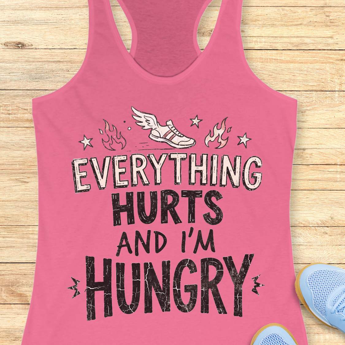 pink tank top with text 'everything hurts and I'm hungry', on a wooden surface