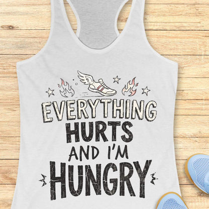 white tank top with text 'everything hurts and I'm hungry', on a wooden surface