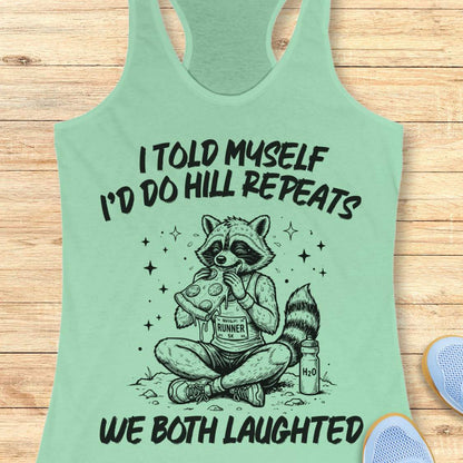 A mint racerback tank top laid flat on a light wood background, featuring a humorous text 'I told myself I'd do hill repeats. We both laughed'.