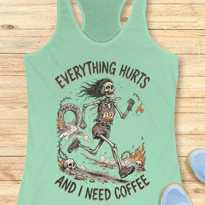 A mint racerback tank top laid flat on a light wood background, featuring a humorous skeleton runner graphic with the text 'everything hurts and I need coffee'.