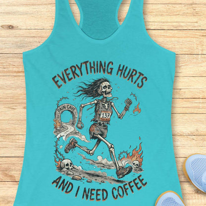 A blue racerback tank top laid flat on a light wood background, featuring a humorous skeleton runner graphic with the text 'everything hurts and I need coffee'.
