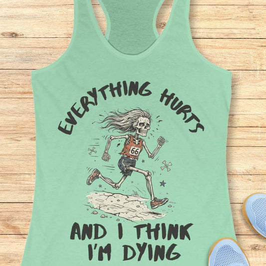 A mint racerback tank top laid flat on a light wood background, featuring a humorous skeleton runner graphic with the text 'everything hurts and I think I'm dying'.
