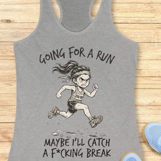 A heather gray racerback tank top laid flat on a light wood background, featuring a humorous female runner graphic with the text 'Going for a run maybe I'll catch a F*cking break'.