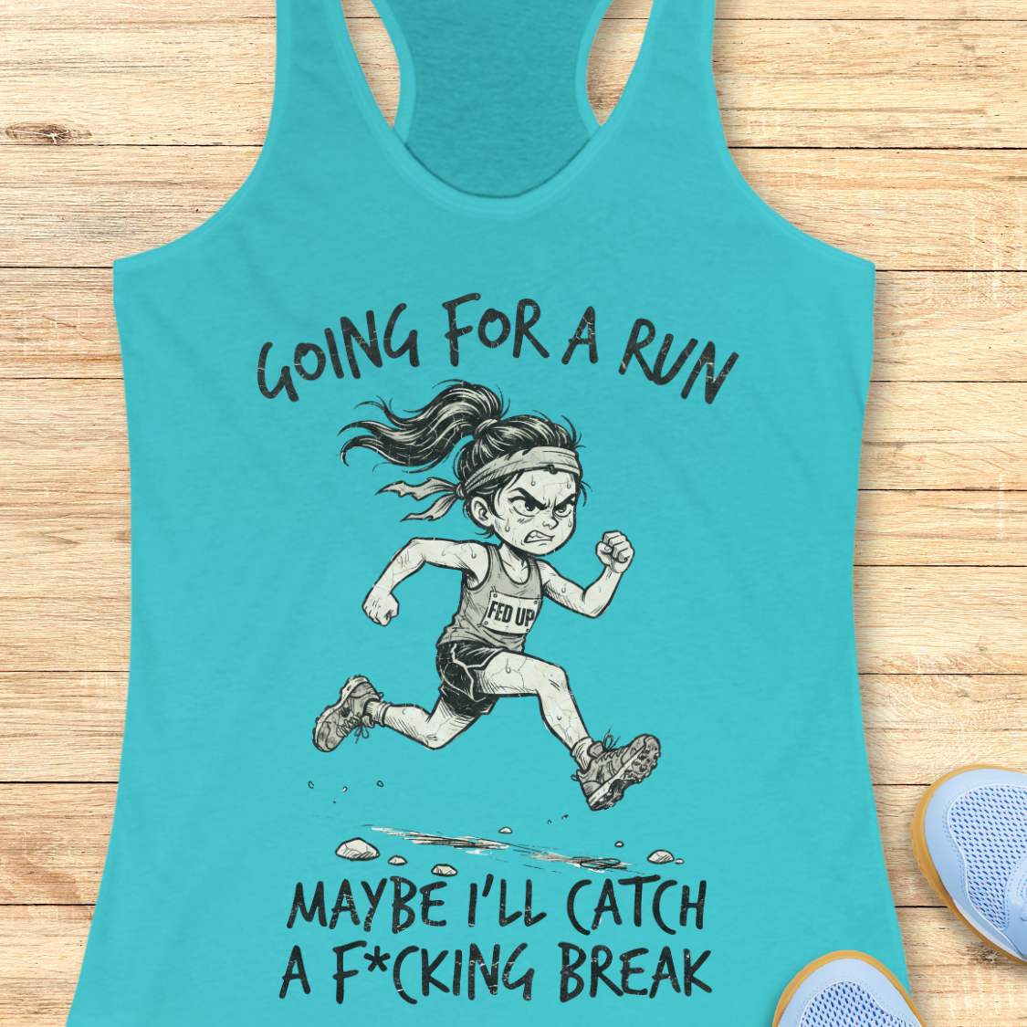 A blue racerback tank top laid flat on a light wood background, featuring a humorous female runner graphic with the text 'Going for a run maybe I'll catch a F*cking break'.