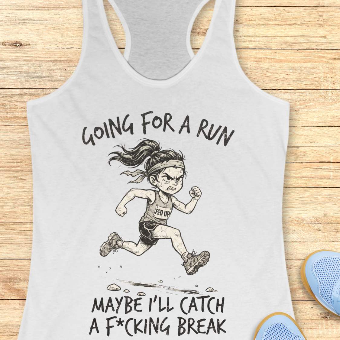 A white racerback tank top laid flat on a light wood background, featuring a black line art illustration of an angry female runner with the text 'GOING FOR A RUN' above and 'MAYBE I'LL CATCH A F*CKING 