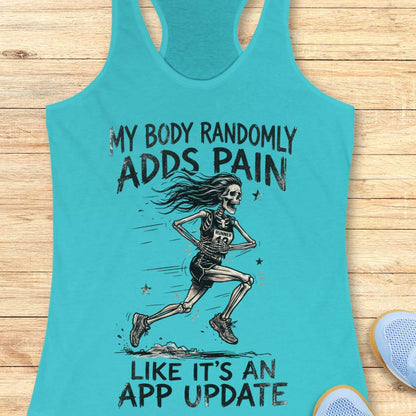 A turquoise racerback tank top laid flat on a light wood surface, featuring a black graphic of a running skeleton and the text 'MY BODY RANDOMLY ADDS PAIN LIKE IT'S AN APP UPDATE'. Part of a blue shoe is visible at the bottom right as a styling prop.