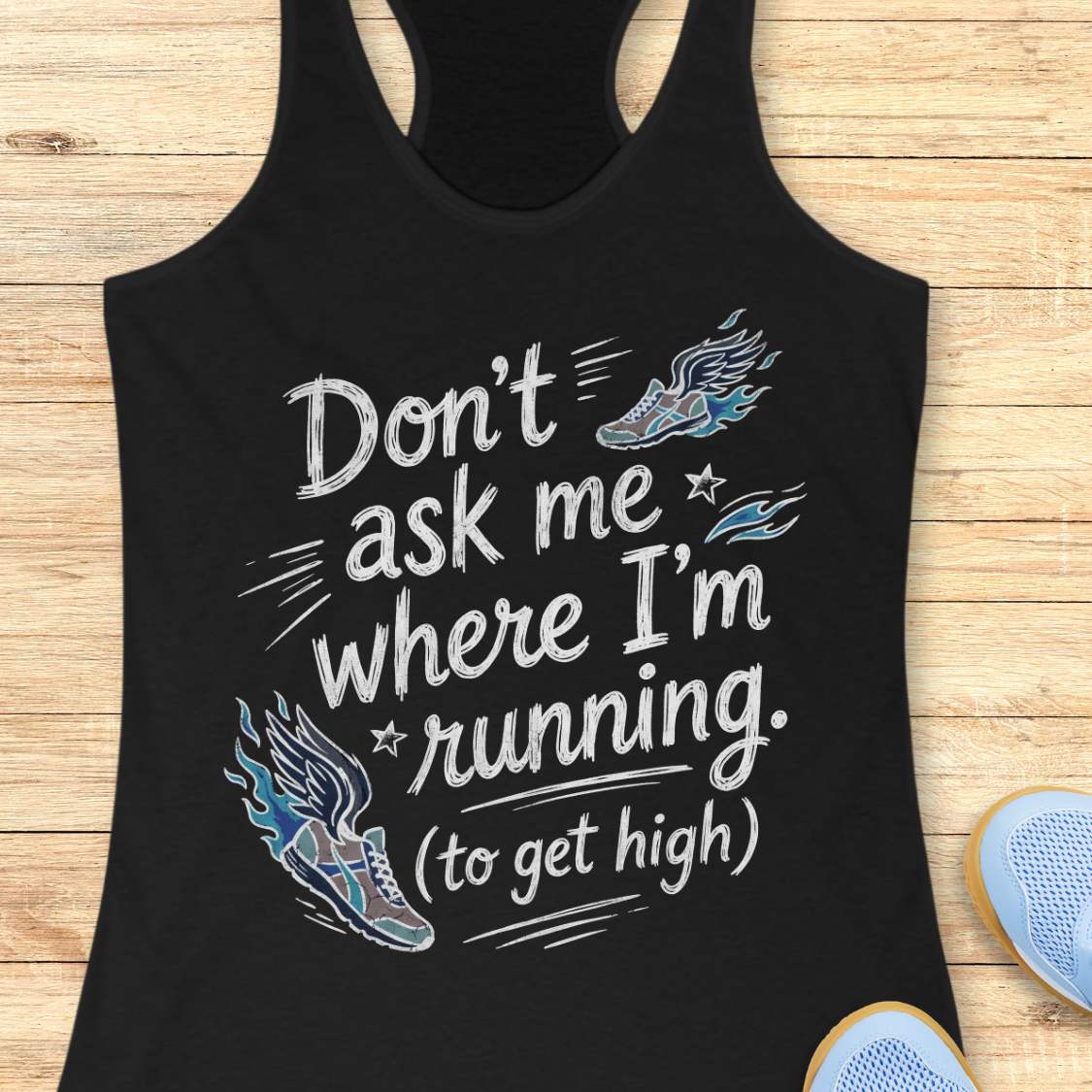 A black racerback tank top with a humorous graphic print reading 'Don't ask me where I'm running. (to get high)' in white, accompanied by blue and white illustrated running shoes, laid flat on a light wood background with partial sneakers visible at the bottom right.