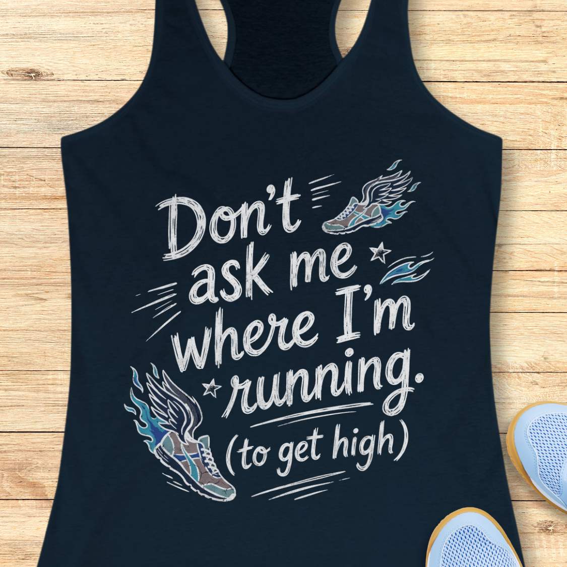 A navy racerback tank top laid flat on a light wood background, featuring a white graphic text print that reads 'Don't ask me where I'm running. (to get high)' with stylized running shoe illustrations in blue, gray, and white.
