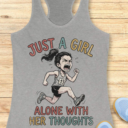 A heather gray racerback tank top laid flat on a light wood background, featuring a graphic of a running girl with the text 'JUST A GIRL ALONE WITH HER THOUGHTS' in multicolored lettering.