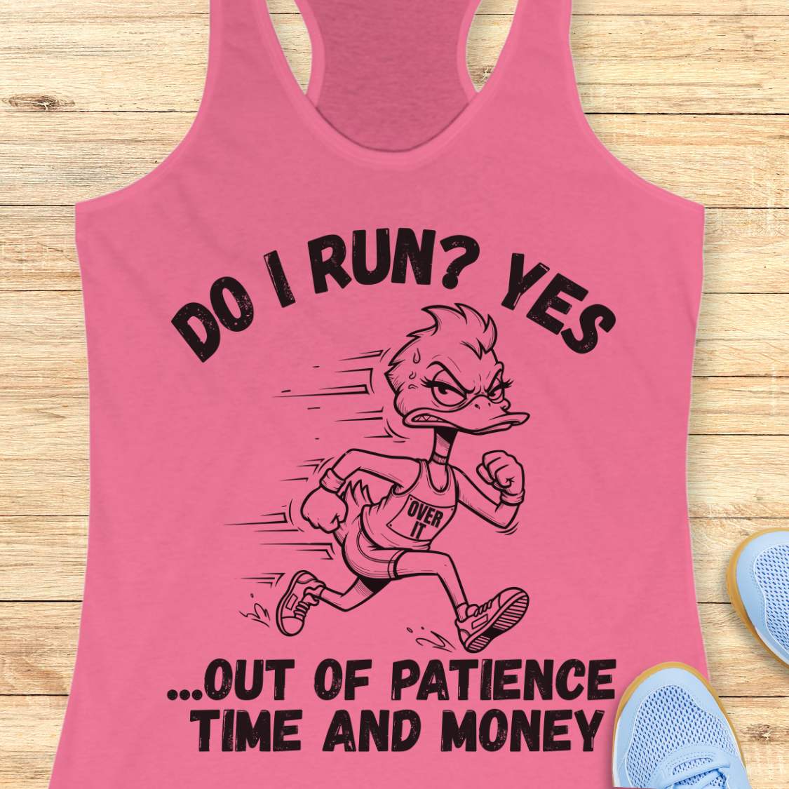 A pink racerback tank top laid flat on a light wood surface, featuring a black graphic of a running duck with the text 'DO I RUN? YES .