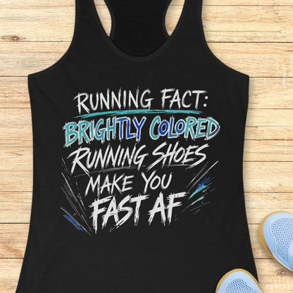 A black racerback tank top laid flat on a light wood surface, featuring a bold graphic text print that reads 'RUNNING FACT: BRIGHTLY COLORED RUNNING SHOES MAKE YOU FAST AF' in white, blue, and teal lettering. Partial light blue sneakers are visible at the bottom right edge.