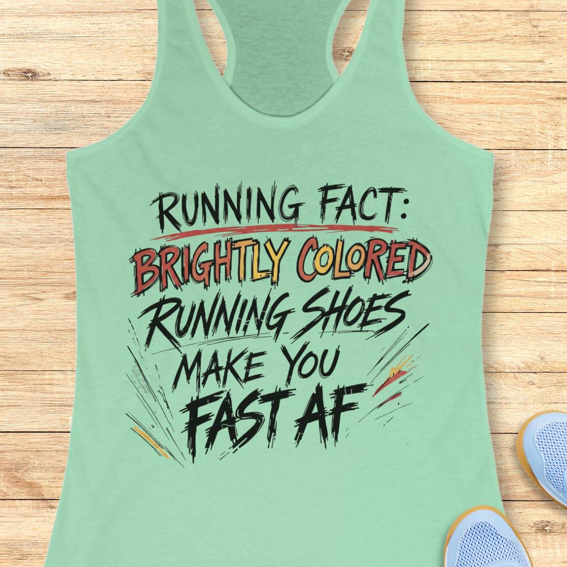 A mint green racerback tank top with a humorous running slogan printed on the front, laid flat on a light wood background with a sneaker partially visible in the corner.