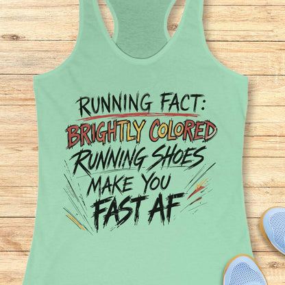A mint green racerback tank top with a humorous running slogan printed on the front, laid flat on a light wood background with a sneaker partially visible in the corner.