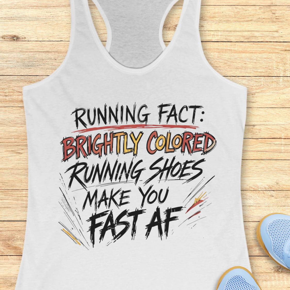 A white racerback tank top with a humorous running slogan printed on the front, laid flat on a light wood background with a pair of blue running shoes partially visible in the corner.