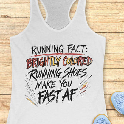 A white racerback tank top with a humorous running slogan printed on the front, laid flat on a light wood background with a pair of blue running shoes partially visible in the corner.