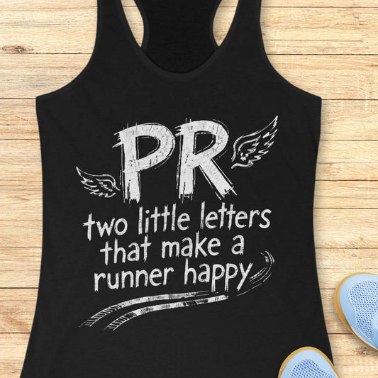 A black racerback tank top laid flat on a light wood surface, featuring a white distressed graphic that reads 'PR two little letters that make a runner happy' with wing illustrations. Partial blue shoes are visible at the bottom right as styling props.