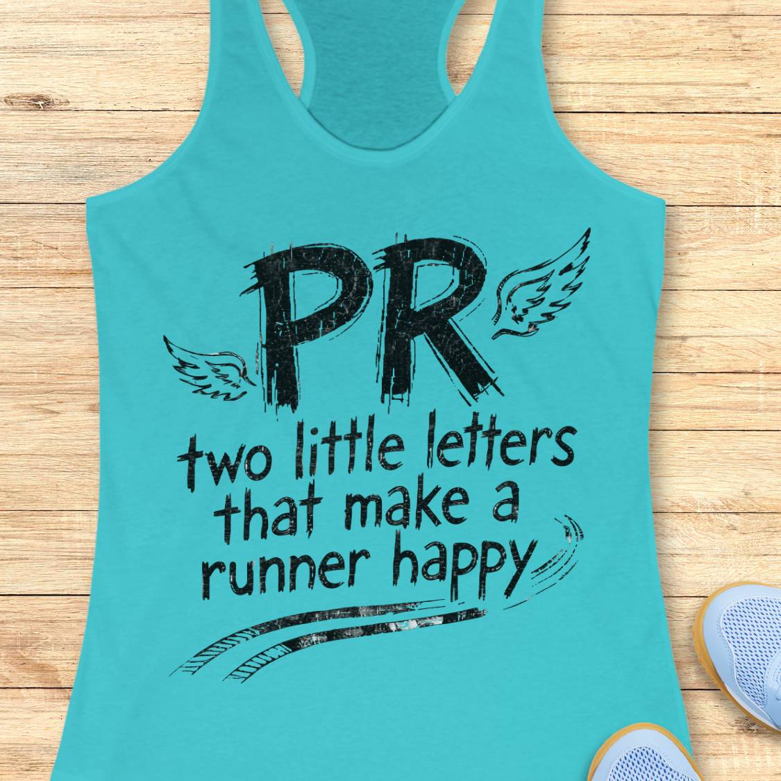 A turquoise racerback tank top with a black graphic print reading 'PR two little letters that make a runner happy' with wings and track lines, laid flat on a light wood background with partial sneakers visible at the edges.
