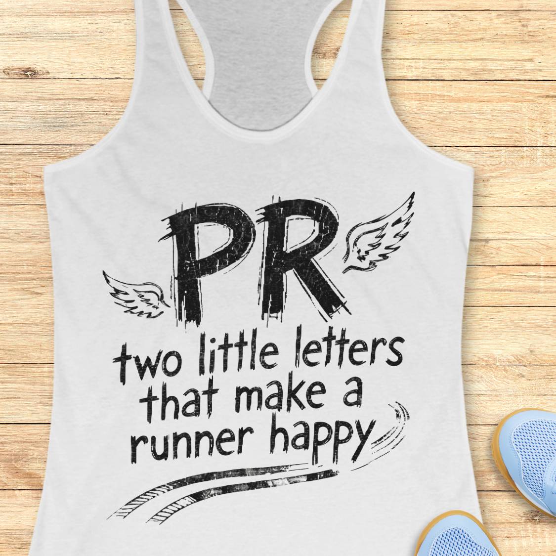 A white racerback tank top with a black graphic print reading 'PR two little letters that make a runner happy' with wing illustrations, shown on a light wood background with partial blue shoes visible at the edges.