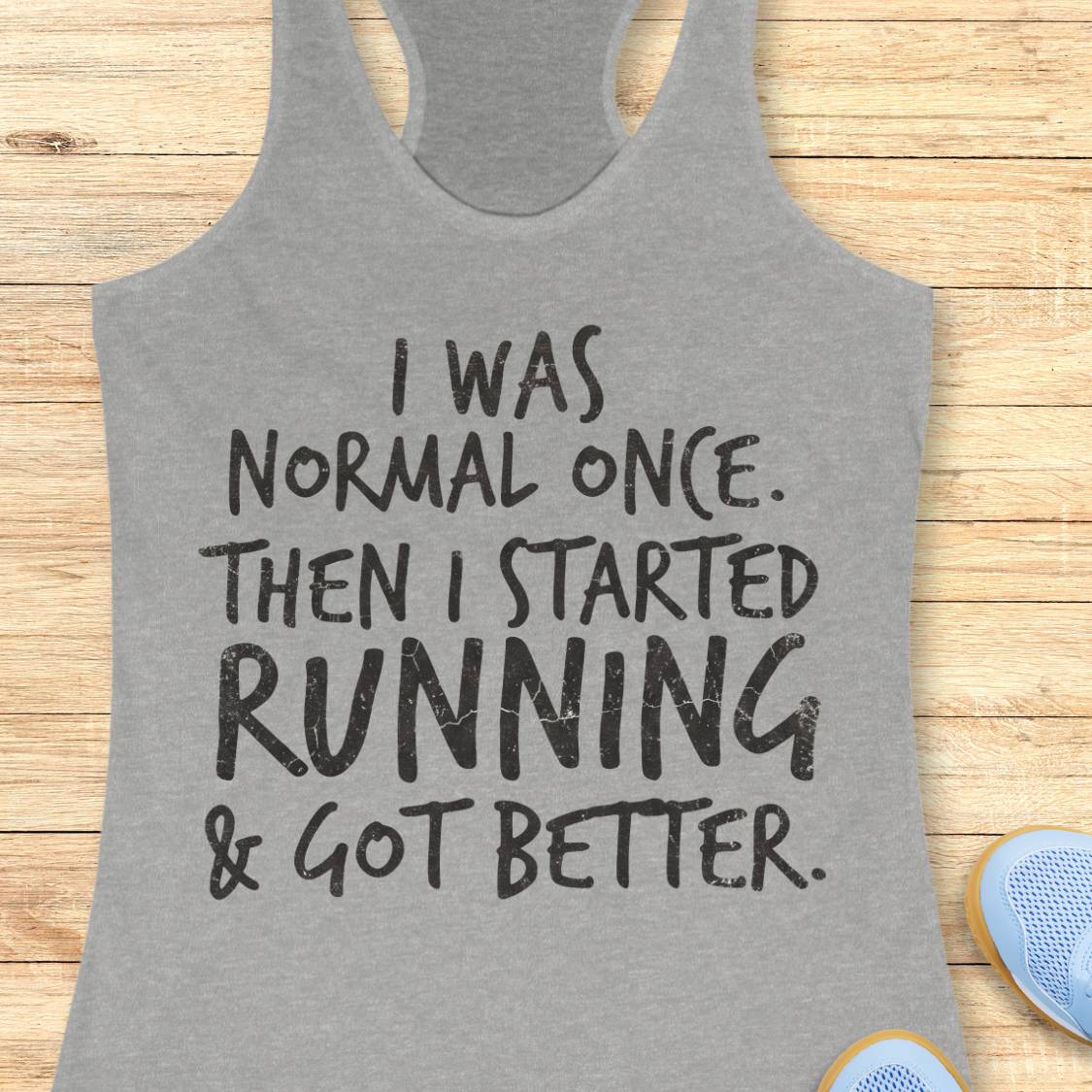 A heather gray racerback tank top with black text reading 'I WAS NORMAL ONCE. THEN I STARTED RUNNING & GOT BETTER.