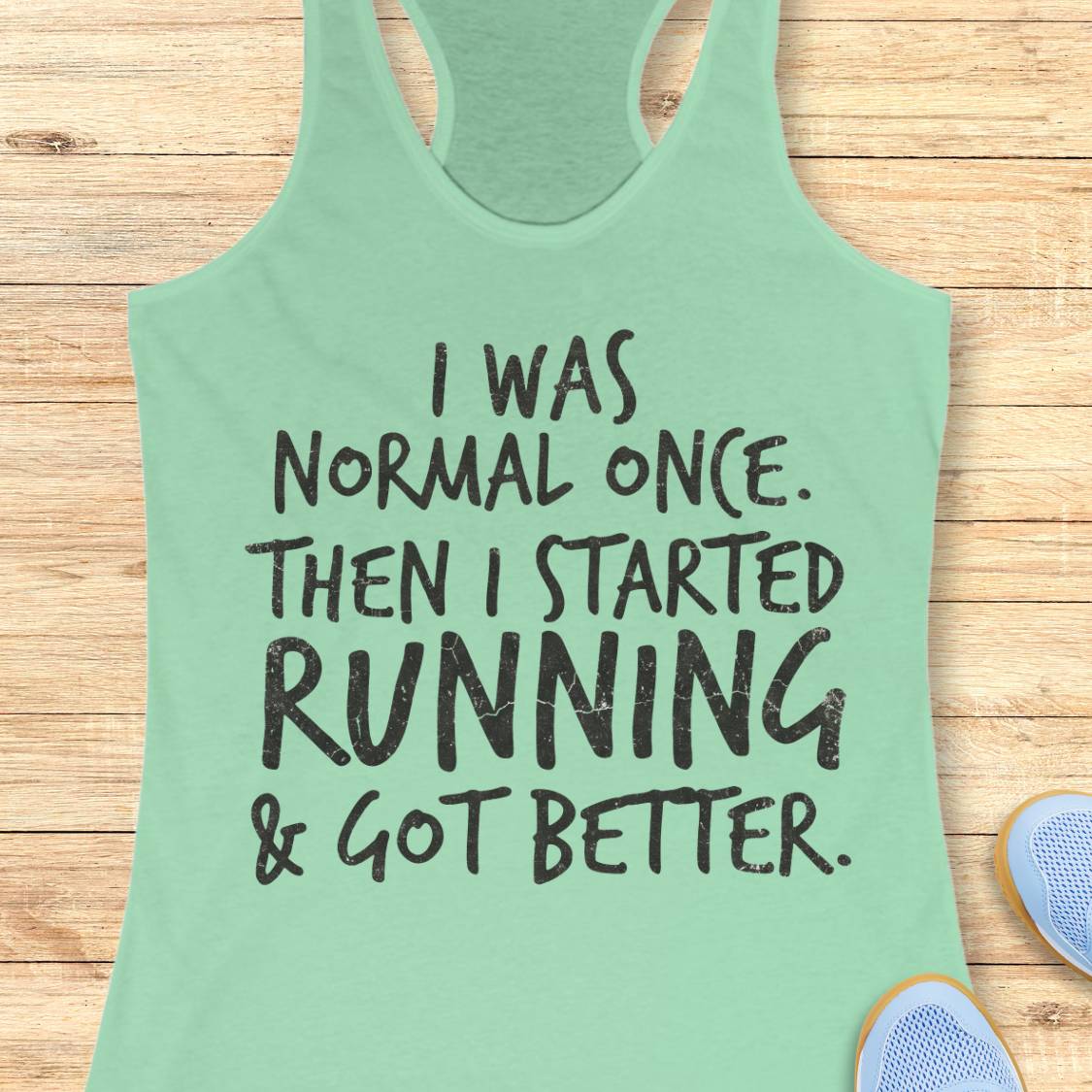 A mint green racerback tank top with black distressed text reading 'I WAS NORMAL ONCE. THEN I STARTED RUNNING & GOT BETTER.