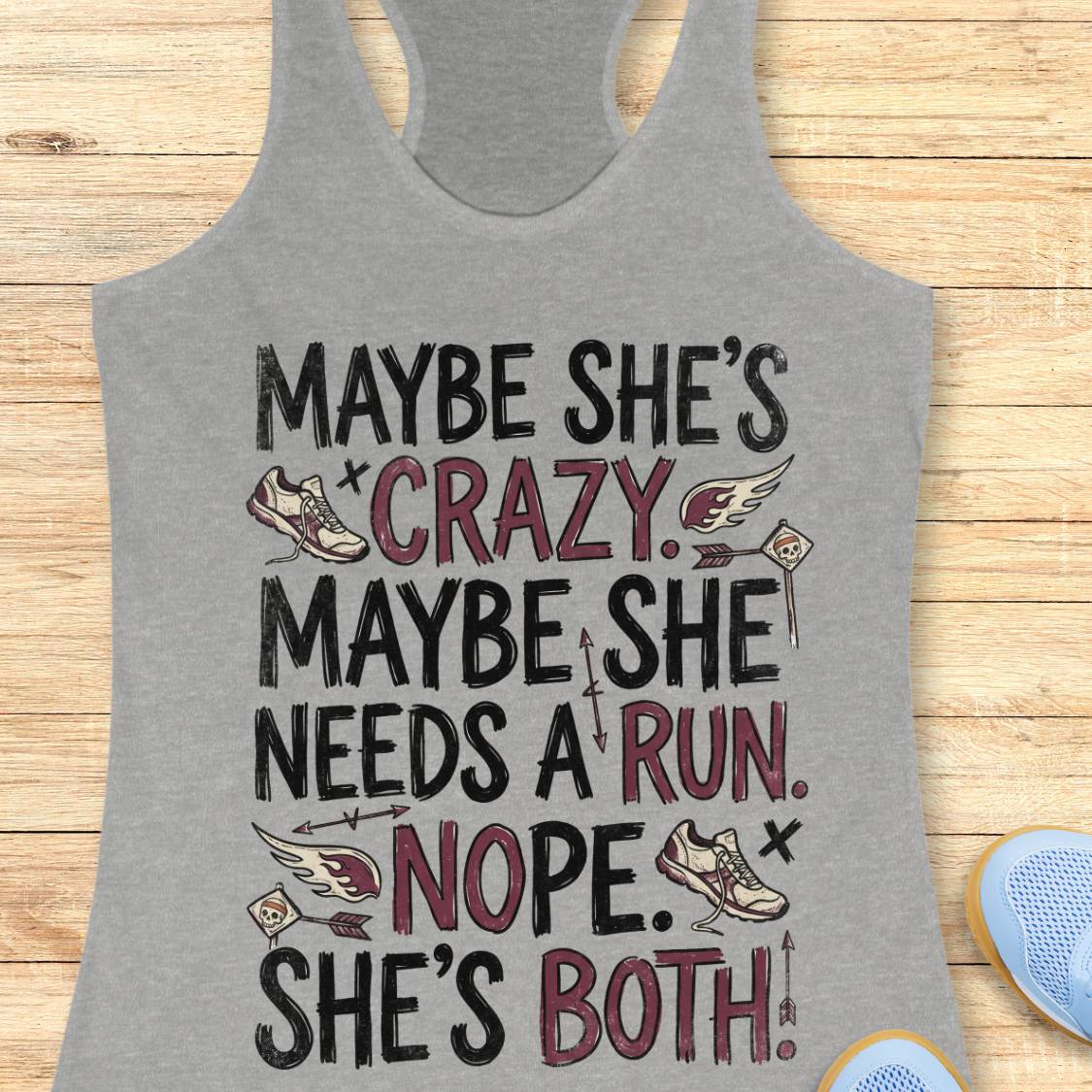 A heather gray racerback tank top with a graphic text print reading 'MAYBE SHE'S CRAZY. MAYBE SHE NEEDS A RUN.