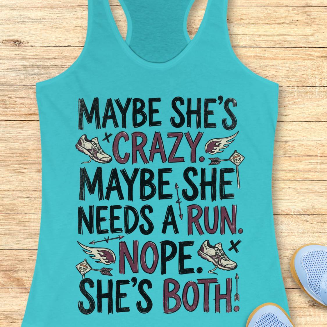 A turquoise racerback tank top laid flat on a light wood surface, featuring a humorous graphic print with the text 'MAYBE SHE'S CRAZY. MAYBE SHE NEEDS A RUN.