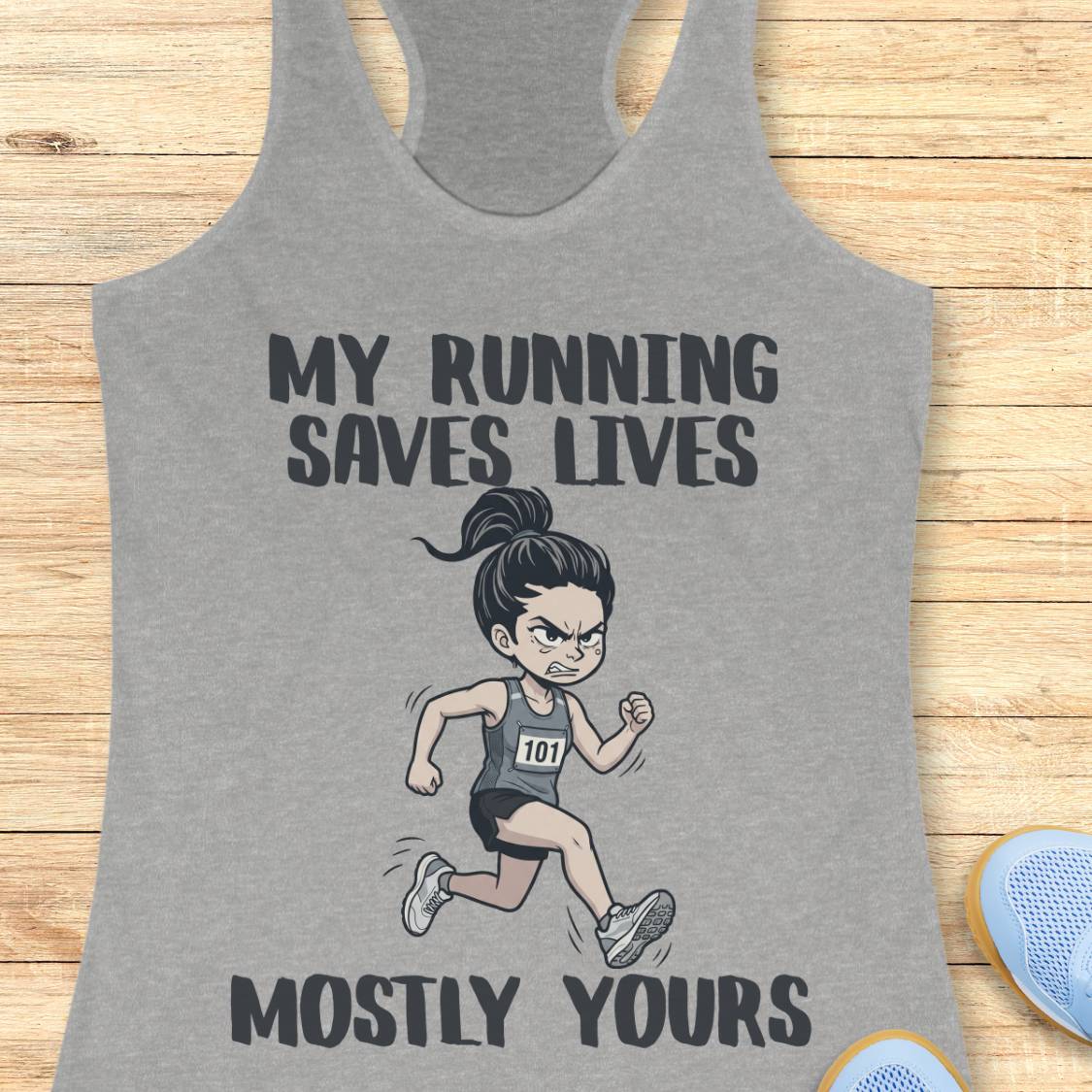 A heather gray racerback tank top laid flat on a light wood background, featuring a cartoon illustration of an angry female runner with the text 'MY RUNNING SAVES LIVES MOSTLY YOURS'.