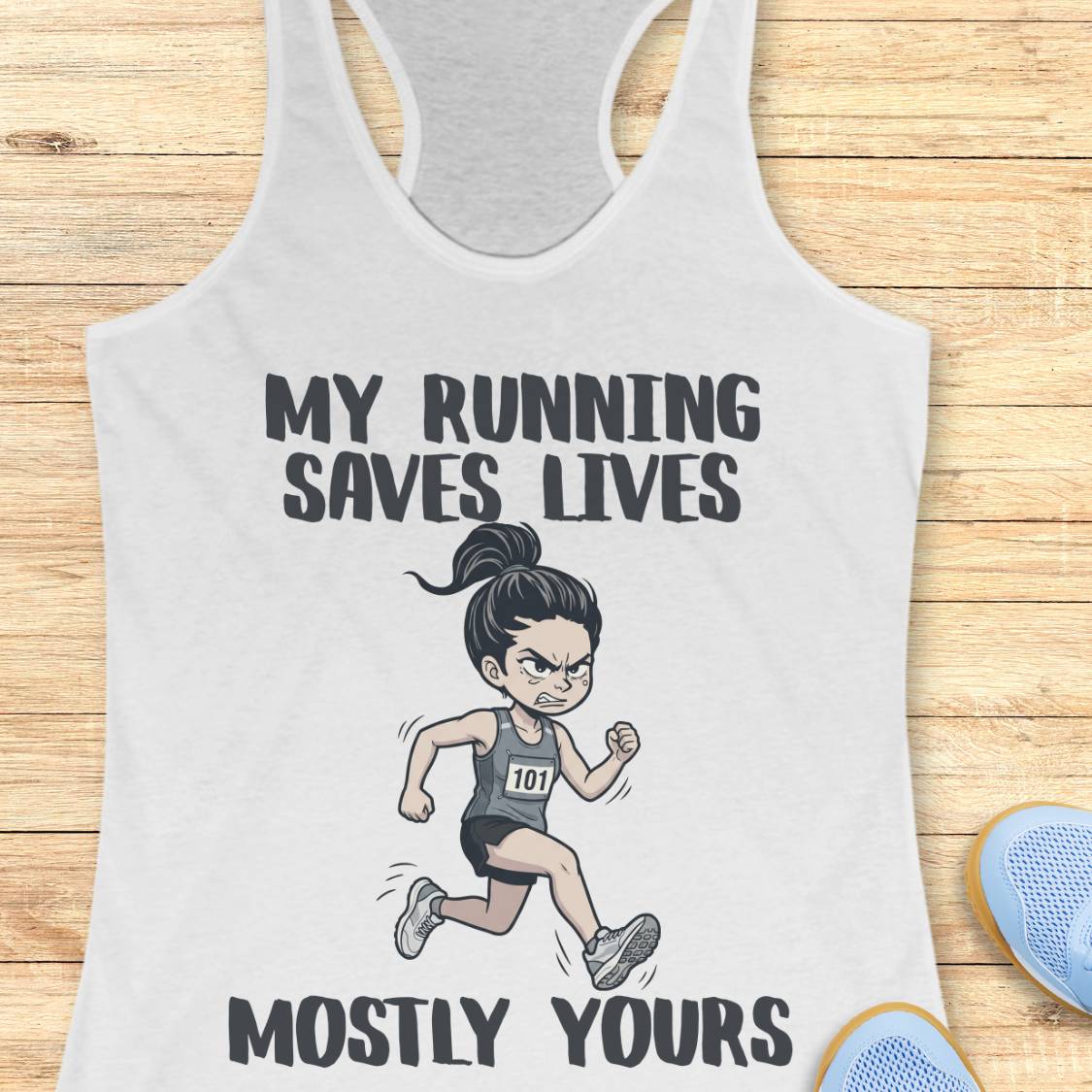 A white racerback tank top laid flat on a light wood surface, featuring a cartoon illustration of an angry female runner with the text 'MY RUNNING SAVES LIVES MOSTLY YOURS' in dark gray lettering. Partial blue shoes are visible at the bottom right as styling props.