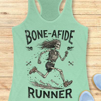 A mint green racerback tank top laid flat on a light wood background, featuring a distressed black graphic of a running skeleton with the text 'BONE-AFIDE RUNNER' and small flying bones around it.