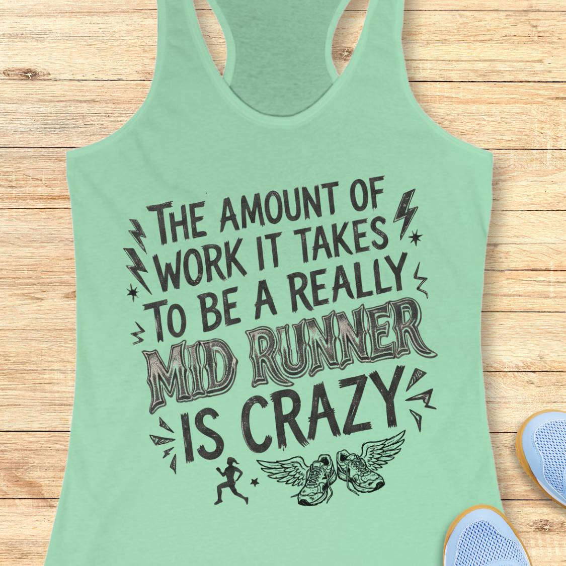 A mint green racerback tank top with a humorous graphic for mid-runners, laid flat on a light wood background with athletic shoes partially visible in the corner.