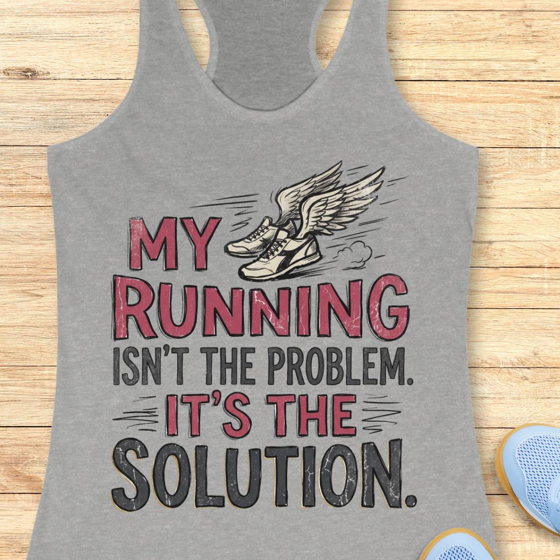 A heather gray racerback tank top laid flat on a light wood background, featuring a graphic print with the text 'MY RUNNING ISN'T THE PROBLEM. IT'S THE SOLUTION.
