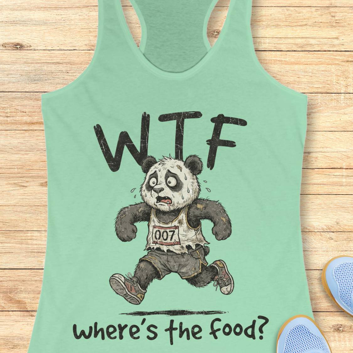 A mint green racerback tank top laid flat on a light wood background, featuring a cartoon panda running with the text 'WTF' above and 'where's the food?' below.