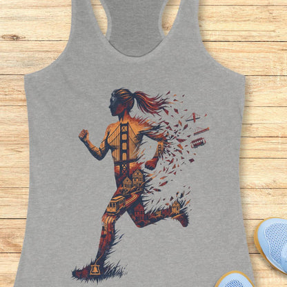 A heather gray racerback tank top featuring a graphic print of a running woman composed of San Francisco landmarks and street elements, laid flat on a light wood plank background.