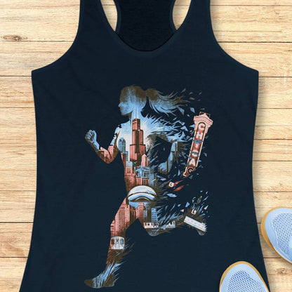 A navy racerback tank top laid flat on a light wood background, featuring a large graphic print of a running silhouette filled with cityscape and architectural details in muted blue, red, and beige tones. Partial white sneakers are visible at the bottom right as styling props.