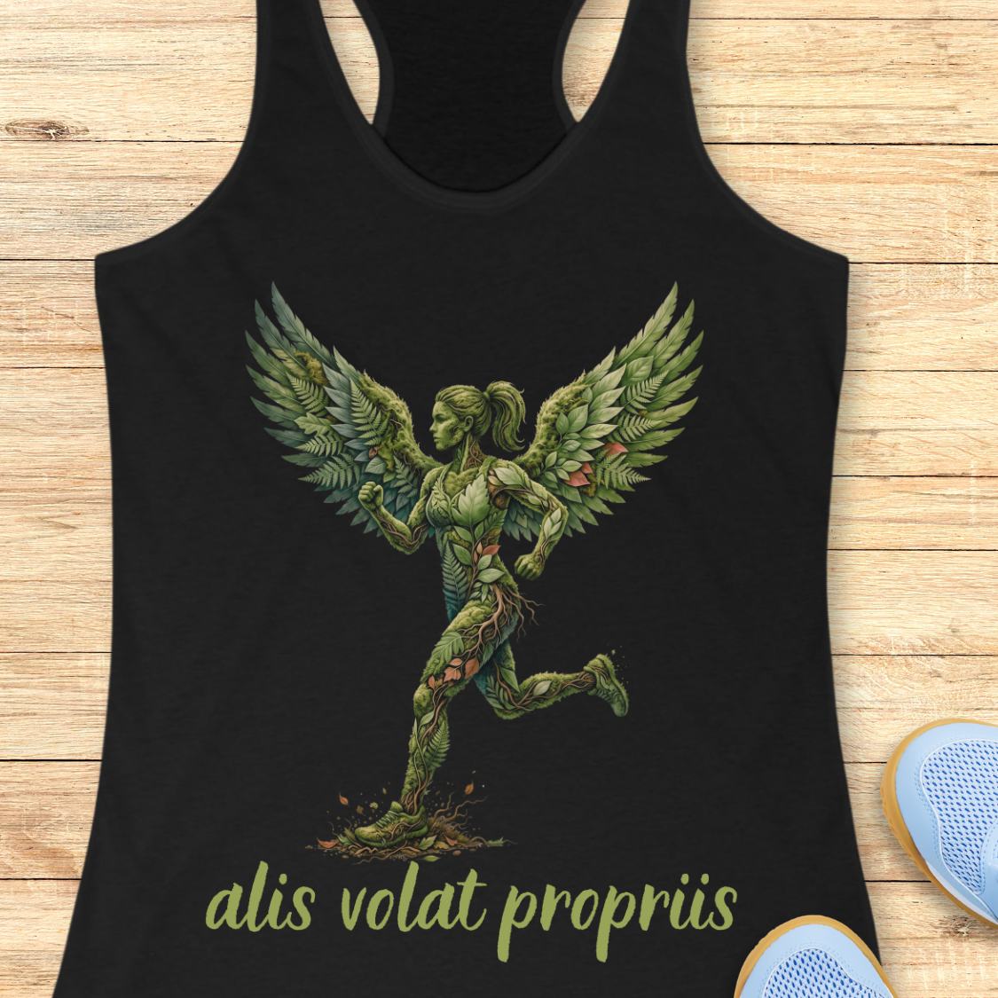 A black racerback tank top laid flat on a light wood surface, featuring a large green winged figure graphic on the front with the text 'alis volat propriis' in green below it. Part of a light blue shoe is visible at the bottom right.