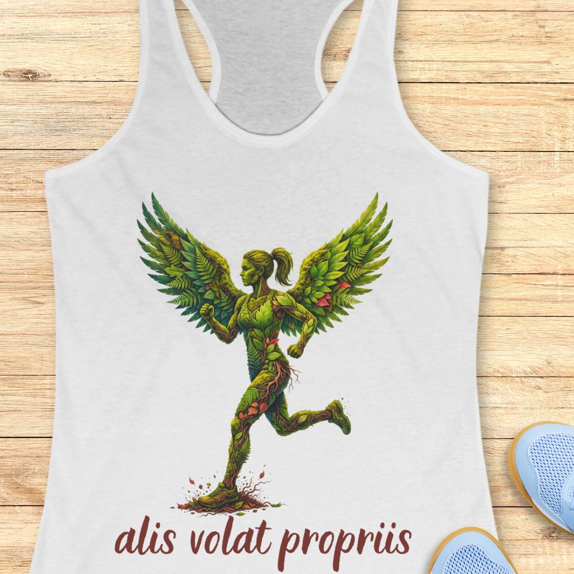 A white racerback tank top featuring a graphic of a winged female figure made of green leaves and vines, with the text 'alis volat propriis' printed below. The tank top is displayed flat on a light wood background with a pair of blue sneakers partially visible in the corner.