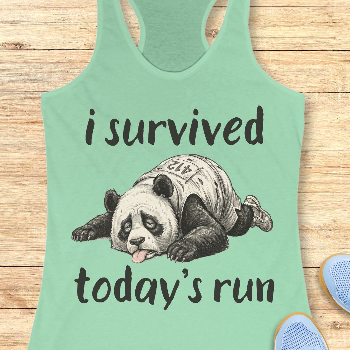 A mint green racerback tank top laid flat on a light wood background, featuring a graphic of a panda wearing a race bib and the text 'i survived today's run'.