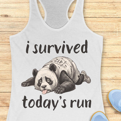 A white racerback tank top laid flat on a wooden surface, featuring a humorous graphic of a panda wearing a race bib and the text 'i survived today's run'.