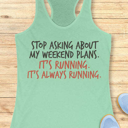 A mint green racerback tank top with a humorous running quote printed on the front, laid flat on a light wood background with partial sneakers visible at the edges.