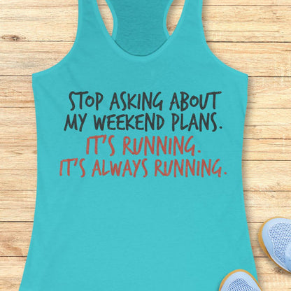 A turquoise racerback tank top laid flat on a light wood floor, with printed text reading 'STOP ASKING ABOUT MY WEEKEND PLANS. IT'S RUNNING.
