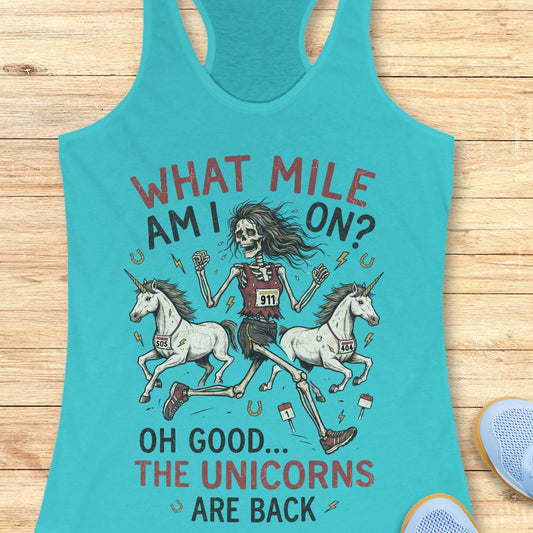 A turquoise racerback tank top laid flat on a light wood surface, featuring a humorous graphic of a skeleton woman racing two white unicorns with the text 'WHAT MILE AM I ON? OH GOOD.