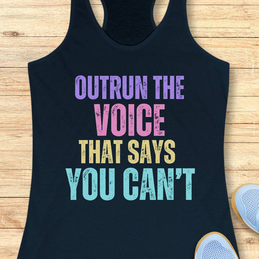 A navy racerback tank top laid flat on a light wood surface, featuring the motivational text 'OUTRUN THE VOICE THAT SAYS YOU CAN'T' in purple, pink, yellow, and light blue distressed lettering. Part of a white sneaker is visible at the bottom right.