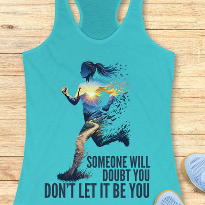 A turquoise racerback tank top laid flat on a light wood surface, featuring a graphic of a running woman with a glowing sunburst and the text 'SOMEONE WILL DOUBT YOU DON'T LET IT BE YOU.' A partial white shoe is visible at the lower right as a styling prop.