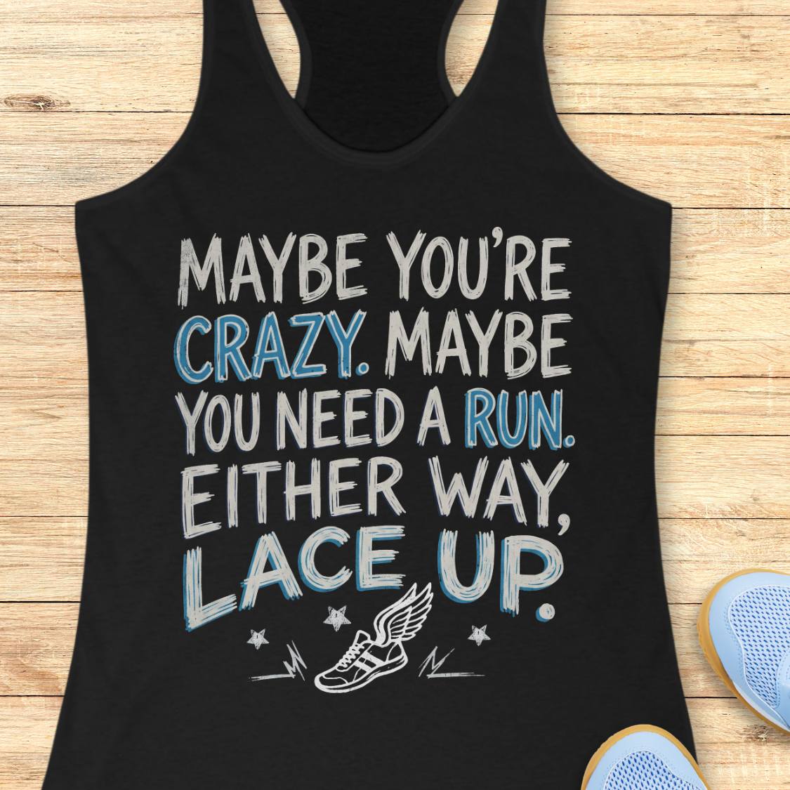 A black racerback tank top laid flat on a light wood background, featuring a motivational graphic that reads 'MAYBE YOU'RE CRAZY. MAYBE YOU NEED A RUN.