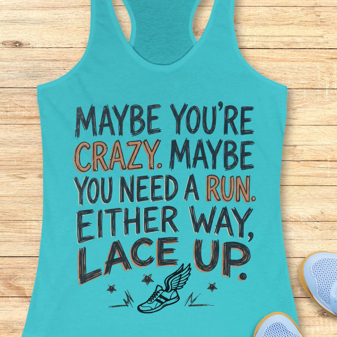 A turquoise racerback tank top laid flat on a light wood background, featuring a motivational running quote in black and orange lettering with a small winged shoe graphic at the bottom. A partial light blue shoe appears at the lower right edge.