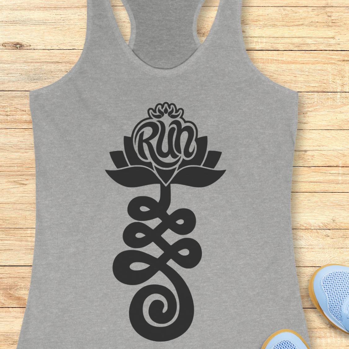 A heather gray racerback tank top with a black graphic of a lotus flower and the word 'Run' integrated into the petals, laid flat on a light wood plank background.