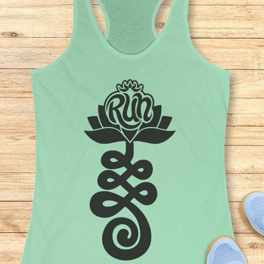 A mint green racerback tank top with a black graphic of a lotus flower and infinity symbol containing the word 'Run', displayed flat on a light wood background with sneakers partially visible at the bottom right.